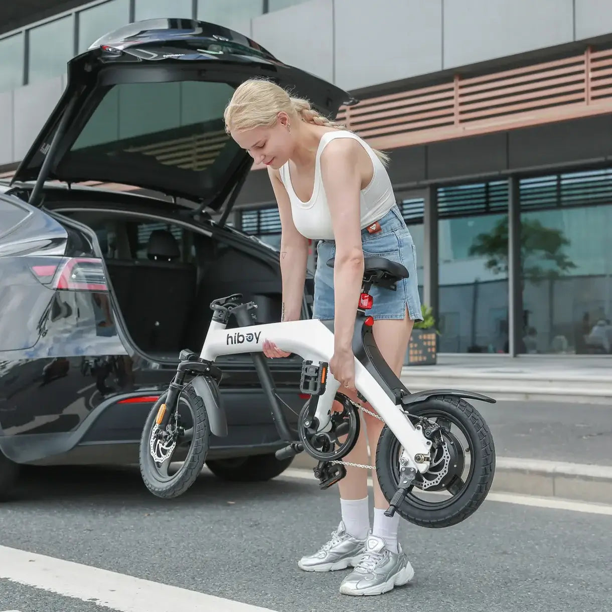 A woman lifting her Hiboy C1 folding e-bike from a car trunk, showcasing its portability and compact design.